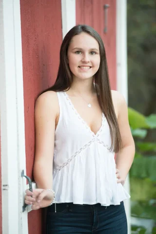 Young woman in a white top standing beside a red barn