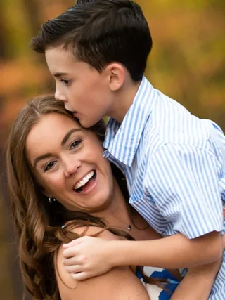 Woman smiling as a boy hugs her and kisses her forehead outdoors