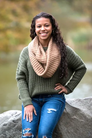 Young woman in a green sweater and tan scarf seated on a rock outdoors